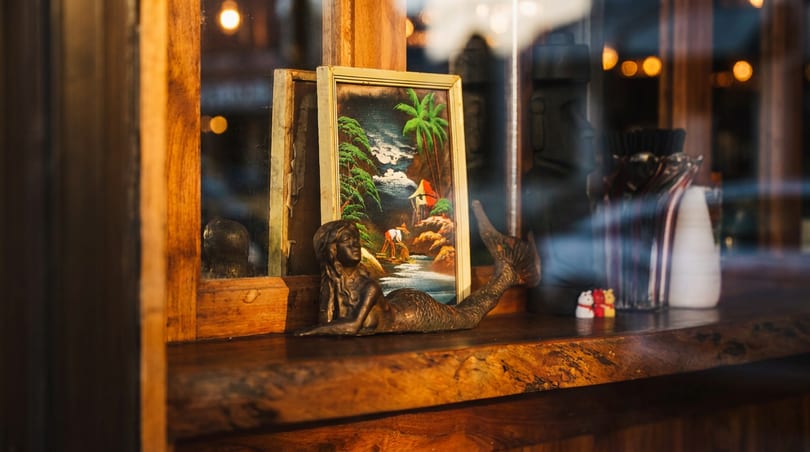 Bronze mermaid statue and tropical painting displayed on a rustic wooden window ledge.