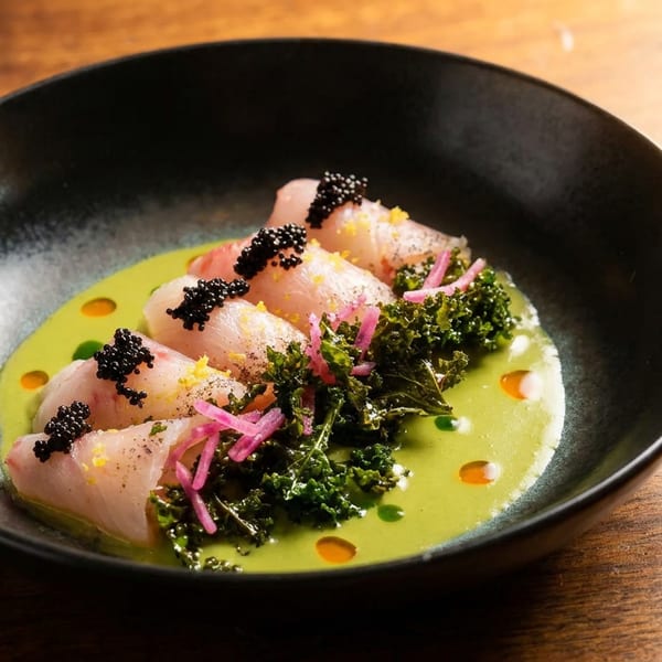 Delicate fish crudo topped with caviar, kale, and pickled onions on a vibrant green sauce.