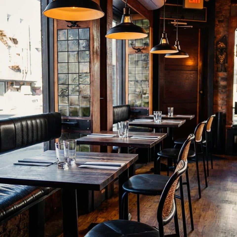 Empty restaurant interior with dark wooden tables, black booths, and warm lighting from pendant lamps.